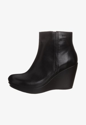 Botines de cuero negro con punta redondeada, tacón alto de cuña y textura suave. Presentan costuras mínimas y una silueta elegante.