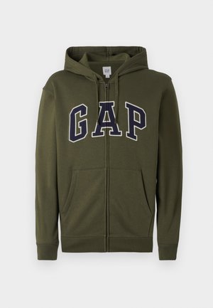 Olijfgroene ritskap met een groot marineblauw 'GAP' logo, twee vo zakken en een trekkoord capuchon. Soepele katoenmix materiaal.