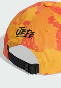 Mütze aus strukturiertem Stoff mit orangefarbenen und gelben pixelierten Mustern. Schwarzes verstellbares Band mit einem Verschluss auf der Rückseite. "Jet"-Logo gestickt.