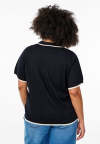 Svart kortärmad t-shirt med vit kant runt kragen och ärmarna, tillverkad av ett mjukt tyg. Avslappnad passform med rundad nederkant.