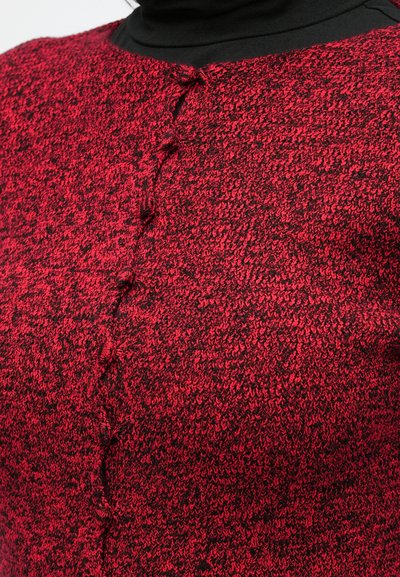 Pletený kardigán z červenej a čiernej priadze, s textúrovaným vzorom a zapínaním na gombíky pri krku. Mäkká tkanina s útulným vzhľadom.
