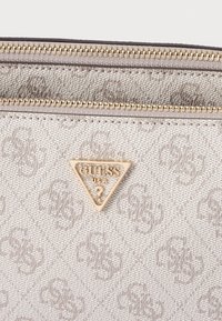 Borsa beige in tessuto testurizzato, con cerniera dorata e piastra logo triangolare in oro. Presenta un motivo delicato su tutta la superficie.