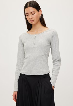 Grå langærmet top i blødt stof med rund halsudskæring, tre teksturerede knapper foran og en lille lap-detalje på siden.