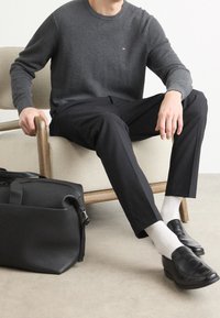 Pullover grigio lavorato a maglia, pantaloni neri, scarpe di pelle nera e calze grigie. Una borsa nera strutturata è accanto a una sedia di legno.