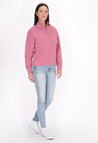 Lichtroze, ritssluiting sweatshirt met een hoge kraag, met een ontspannen pasvorm en lange mouwen. Gecombineerd met lichtblauwe skinny jeans en witte sneakers.