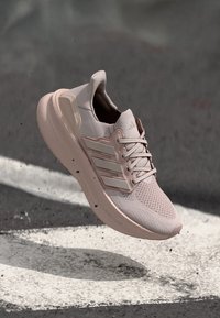 Lys rosa treningssko med mesh-overdel, tre hvite striper, gummisåle og snøring, med polstret hæl og teksturert design.