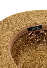 Brązowy pleciony kapelusz przeciwsłoneczny z materiałowym paskiem na potylicę i regulowanym wiązaniem, z czarną metką "KOLLEKCJA PARFOIS" w środku.