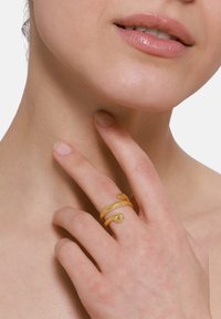 Bague dorée au design de serpent avec des écailles texturées et une petite pierre en accent. Portée sur un doigt avec une finition d'ongle naturel.