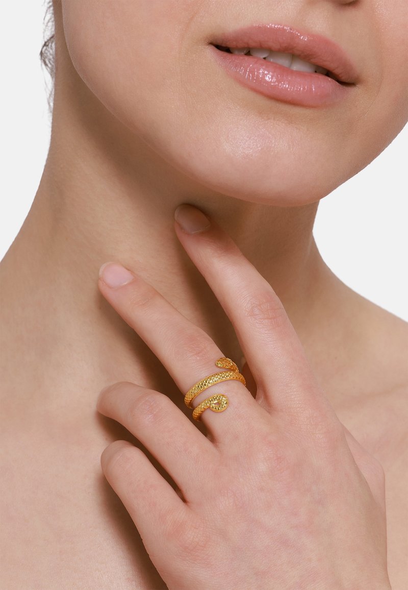 Bague dorée au design de serpent avec des écailles texturées et une petite pierre en accent. Portée sur un doigt avec une finition d'ongle naturel.