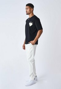 Camiseta de algodón negra con un diseño de corazón en el pecho, combinada con pantalones blancos y zapatillas blancas. Ajuste sencillo y relajado.