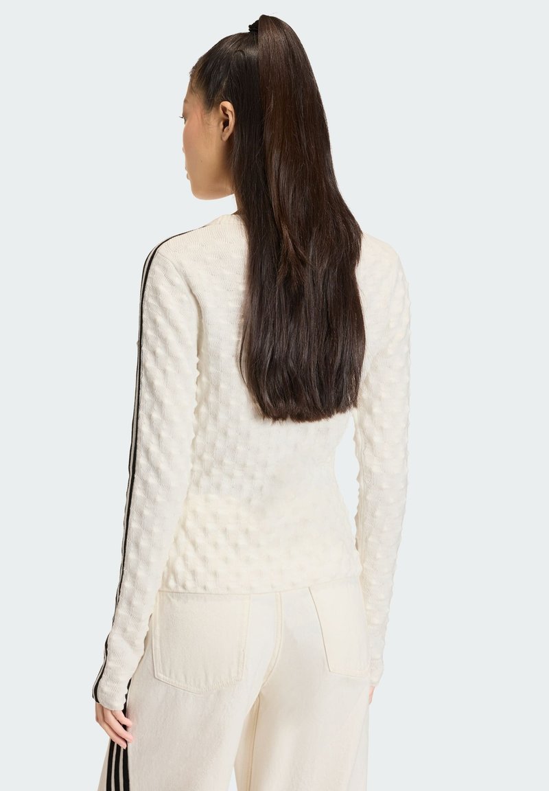 Weißer strukturierter Pullover mit langen Ärmeln und schwarzen Seitenstreifen. Das Design umfasst eine taillierte Silhouette und einen Rundhalsausschnitt.