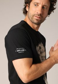T-shirt noir à manches courtes avec un imprimé graphique et une étiquette sur la manche gauche ; en coton, col rond, coupe medium.