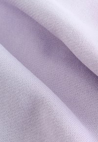 Tissu tissé violet clair avec une texture lisse, présentant un motif de tricot fin et des variations subtiles de couleur et de lumière.