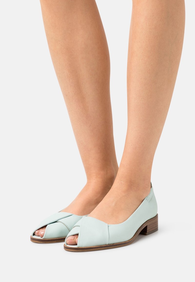 Chaussures en cuir bleu clair avec un design à bouts ouverts et un petit talon carré. Elles présentent des brides croisées à l'avant et une finition lisse.