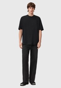 Sort t-shirt med korte ærmer i løs pasform, med rund halsudskæring og diskret logo på brystet. Kombineret med mørke jeans med lige ben.