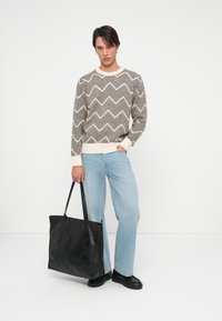 Sivi i kremasti džemper s cik-cak uzorkom, svijetloplave traperice, crna kožna torba, crne cipele, jednolična bijela pozadina.