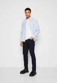 Camisa de botones a rayas azul claro sobre una camiseta blanca, combinada con unos vaqueros oscuros y zapatos de plataforma negros. Diseño simple y casual.