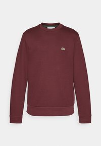 Sudadera burdeos hecha de una tela suave, con un escote redondo, puños acanalados y un pequeño logo verde en el pecho.