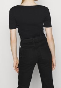 Černý top s krátkým rukávem s přiléhavým střihem a nařasenou texturou v pase, kombinovaný s černými džínami s vysokým pasem a zadními kapsami.