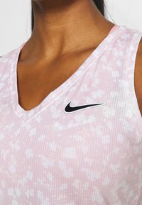 Růžové bezrukávové sportovní tričko s výstřihem do V, s texturovaným vzorem a černým logem Nike na levé části hrudi.