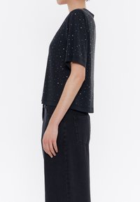 Černý top s krátkým rukávem, zdobený rozptýlenými vícolorovými cvočky, jednoduchým střihem a volným fit, doplněný černými džínami s vysokým pasem.