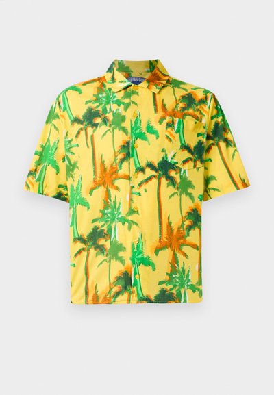 Dzeltena īsām piedurknēm kunga krekls ar zaļiem un oranžiem palmu kokiem un priekšējo krūšu kabatu, izlikts plakans uz baltas fona.