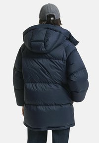 Gevoerde marineblauwe pufferjack met capuchon, met een quilted ontwerp en een loose fit. De stof lijkt glad en waterafstotend.