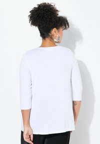 Maglietta bianca a maniche lunghe con vestibilità rilassata, scollatura rotonda e texture morbida. Presenta maniche a tre quarti e orlo curvo.