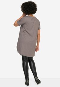 Tunique grise à manches courtes avec une coupe ample, dotée d'un ourlet arrondi. Associée à des leggings noirs ajustés et des chaussures noires à clous.