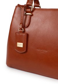 Borsa a mano in pelle marrone con texture liscia, accessori in metallo dorato e un'etichetta removibile con il marchio "Hexagona."