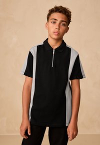 Černé polo tričko se šedými bočními akcenty, krátkými rukávy a zipem u krku. Vyrobené z bavlny, má hladkou texturu.