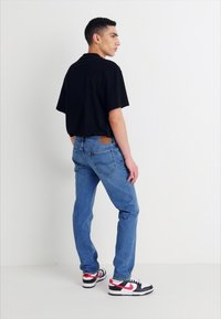 Črna majica s kratkimi rokavi, svetlo modri jeans z zadnjimi žepi in črnimi, rdečimi in belimi supergami. Preprost dizajn, sproščen kroj.