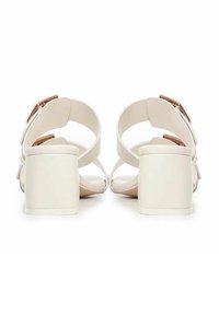 Sandali con tacco in beige chiaro, caratterizzati da cinturini incrociati e tacco a blocco. Accentuati da dettagli in metallo dorato sui cinturini.