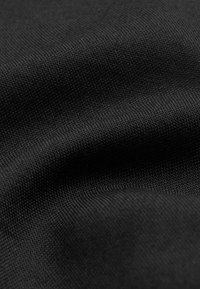 Zbliżenie na czarną tkaninę o widocznej fakturze i subtelnych fałdach tworzących delikatne cienie i refleksy.