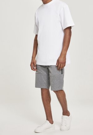 T-shirt en coton blanc à manches courtes, associé à un short gris texturé avec des poches zippées et des baskets blanches.