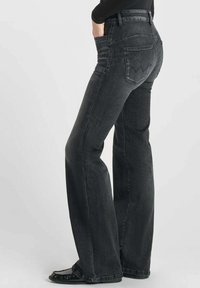 Pantalones vaqueros negros acampanados de mezclilla con bolsillos frontales, costuras en contraste y un diseño distintivo en el bolsillo trasero. Textura suave.