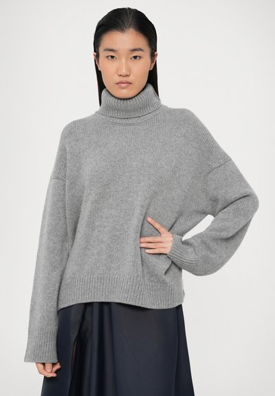 Pullover grigio con collo alto in morbido knit, vestibilità oversized con spalle a caduta, polsini e orlo a costine, caratterizzato da una tasca laterale.