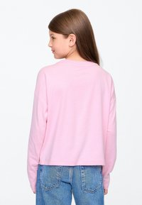 Világos rózsaszín, hosszú ujjú, rövidített fazonú ing puha pamutból, kerek nyakkivágással és laza szabással, kék farmerral párosítva.