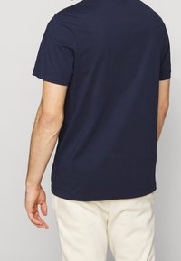 Navy blue cotton t-shirt with short sleeves, crew neck, and a relaxed fit, worn with light-colored trousers. Simple, solid design.