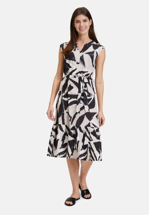 Schwarz-weiß gemustertes Kleid mit einem Kordelzug in der Taille, kurzen Ärmlen und einem plissierten, gestuften Rock. Hergestellt aus leichtem Stoff.