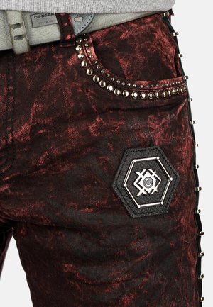 Black and red patterned denim jeans with silver stud accents, hexagonal patch, and textured details on the side. Belts included.