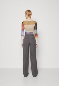 Maglia a maniche lunghe multicolore con un design a gradiente in tonalità di arancione, viola e giallo. Abbinata a pantaloni grigi a vita alta.
