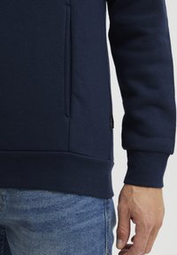 Felpa blu navy con tasca a marsupio, polsini e orlo a coste. Tessuto morbido, con un piccolo etichetta del marchio sul lato.
