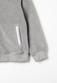 Felpa grigia con finitura strutturata, dotata di una tasca laterale con dettagli bianchi, polsini a costine e logo sulla manica.