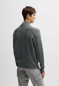 Gray ribbed sweater with a high collar, featuring long sleeves and a fitted waist. The texture is smooth and knit with vertical stripes.
