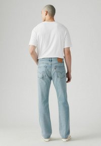 Helle blaue Straight-Leg-Jeans mit einem Markenpatch aus Leder, Gesäßtaschen mit Stickdetails, getragen mit einem schlichten weißen T-Shirt.