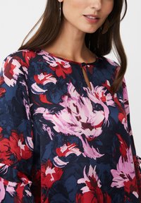 Blumenbluse mit Schlüssel Ausschnitt, mit großen roten und rosa Blumen auf navy Hintergrund, aus strukturiertem Stoff gefertigt.