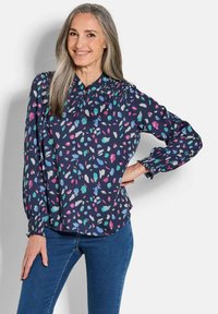 Marineblouse met kleurrijke abstracte patronen in roze, teal en wit. Kenmerkt zich door een gerimpelde hals en elastische manchetten. Langmouwen ontwerp.