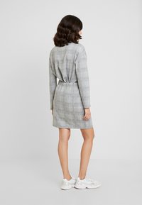 Abito a quadri grigio con vestibilità rilassata, maniche lunghe e vita elastica, abbinato a scarpe da ginnastica bianche. Tessuto dalla texture morbida.