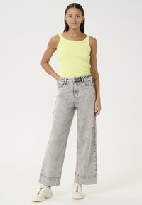 Top a fascia giallo neon a coste abbinato a jeans a gamba larga grigi con vita alta e orlo sfrangiato, indossato con sneakers bianche.